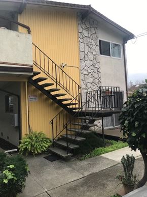Oakland apartment for rent - A yellow house with a stone wall and a black metal staircase.