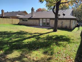 Tulsa house for rent - A house with a brown roof and a stone chimney is surrounded by a grassy lawn with fallen leaves.
