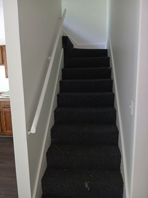 Louisville apartment for rent - A staircase with black carpeted steps and white handrails.