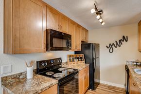 Clackamas apartment for rent - Apartments Happy Valley, OR - Sunnyside Village - a Kitchen with Wood-Style Flooring, Granite Countertops, Black Appliances Including a Refrigerator, Oven, Dishwasher, and Built-In Microwave, Brown Wood-Style Cabinetry, and an Overhead Lighting Fixture