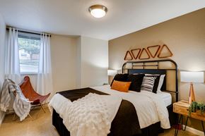 Clackamas apartment for rent - One Bedroom Apartments in Happy Valley, OR - Sunnyside Village - a Bedroom with Plush Carpeting, a Bed, Two Bedside Tables with Lamps, a Ceiling Lamp, and a Window with Binds and Curtains