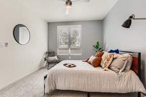 Portland apartment for rent - 1-Bedroom Modern Apartments in Downtown Portland, OR - Linc 245 - Bedroom with Carpet Flooring, Large Bed, Mirror, Lamp, Chair, and Ceiling Fan.