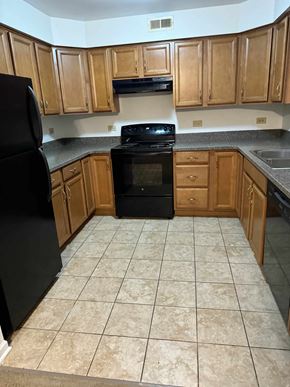 Lisle apartment for rent - A black refrigerator is in a kitchen with wooden cabinets.