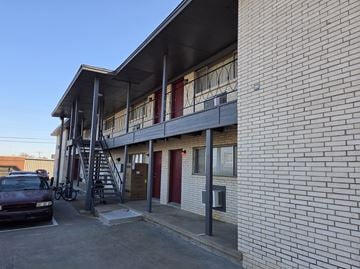 Tulsa apartment for rent - A red car is parked in a parking lot next to a building with a staircase leading to the second floor.