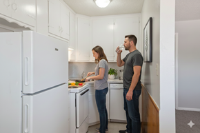 Tulsa apartment for rent - A man and woman are standing in a kitchen with white cabinets and appliances.