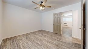 Tulsa apartment for rent - A room with a ceiling fan and light, hardwood floors, and a door leading to another room.