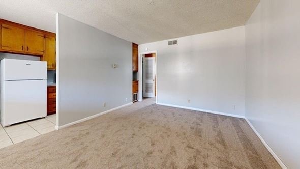 Tulsa apartment for rent - A white refrigerator is in a kitchen with a white wall and a brown carpet.