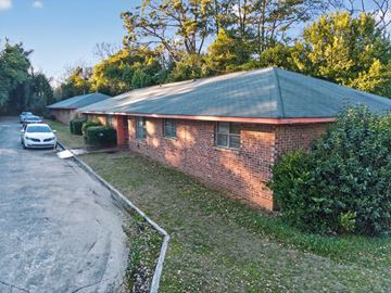 Macon apartment for rent - A red brick building with a green roof is surrounded by greenery.