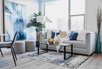 Regina apartment for rent - A living room with a grey couch, a blue rug, and a large painting on the wall.