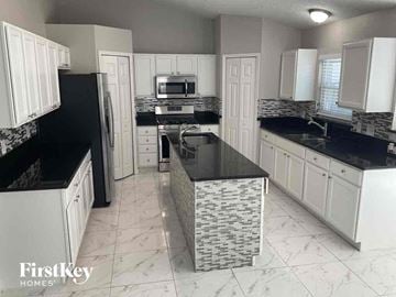 Jacksonville house for rent - a kitchen with white cabinets and black counter tops