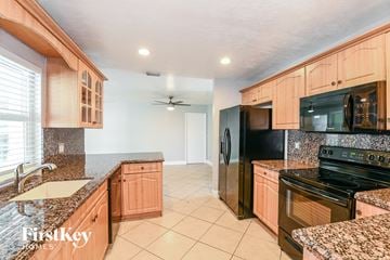 Cape Coral house for rent - a kitchen with wood cabinets and black appliances and granite counter tops
