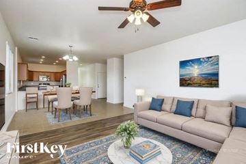 San Tan Valley house for rent - A living room with a beige couch, a dining table with chairs, a ceiling fan, and a painting on the wall.