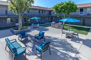 Norwalk apartment for rent - an outdoor patio with blue chairs and umbrellas and a building in the background