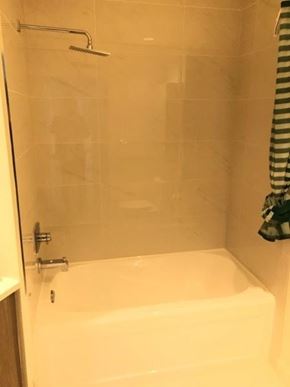 Vancouver apartment for rent - A white bathtub with a shower head and a striped towel hanging on the shower rod.