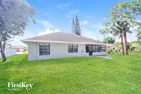 Palm Bay house for rent - A white house with a brown roof is surrounded by green grass and trees.