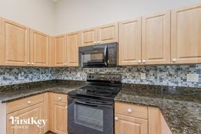 Lehigh Acres house for rent - a kitchen with wood cabinets and black appliances and granite counter tops