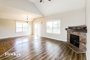 Basehor house for rent - A spacious living room with wood flooring and a stone fireplace.