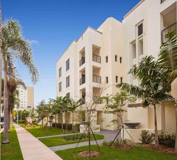 Coral Gables apartment for rent - A modern building with a white exterior and balconies is surrounded by greenery and a walkway.