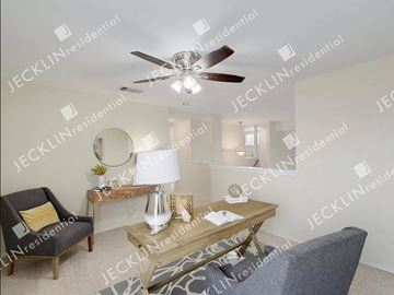 Hutto house for rent - A living room with a ceiling fan, a chair, a table with a lamp and a vase on it, and a mirror on the wall.