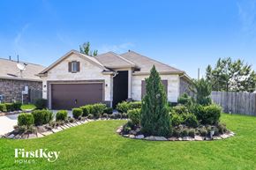 Splendora house for rent - A house with a brown roof and a garage door is surrounded by a well-manicured lawn and a small garden.