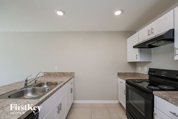 Cape Coral house for rent - a kitchen with white cabinets and black appliances and a sink