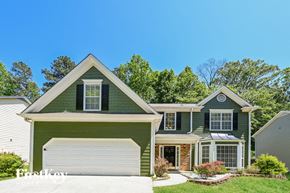 Lilburn house for rent - A green house with a white garage door and a brick chimney.