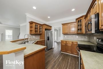 Advance house for rent - a kitchen with wooden cabinets and stainless steel appliances and white counter tops