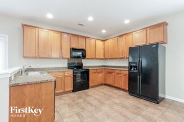 Monroe house for rent - a kitchen with wooden cabinets and a black refrigerator