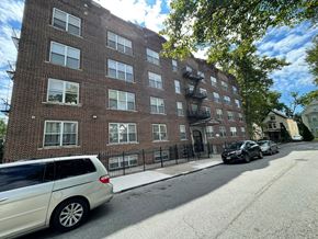 East Orange apartment for rent - A white car is parked on the side of a street in front of a brick building.