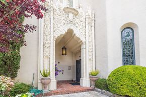 Oakland apartment for rent - A white building with a large arched doorway and a green hose on the left.