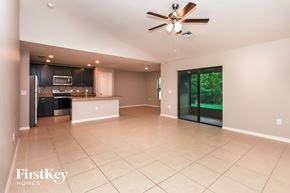 North Port house for rent - A spacious living room with a kitchen in the background and a sliding glass door leading to a backyard.