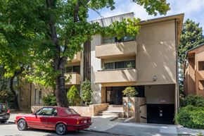 Oakland apartment for rent - A red car is parked in front of a tan building.