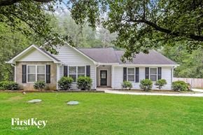 Newnan house for rent - A white house with a black door and windows is surrounded by greenery.