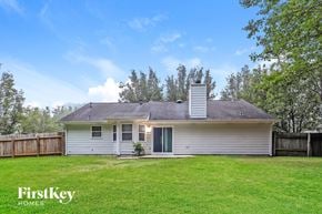 Newnan house for rent - A house with a grey roof and a chimney is surrounded by a green lawn and trees.
