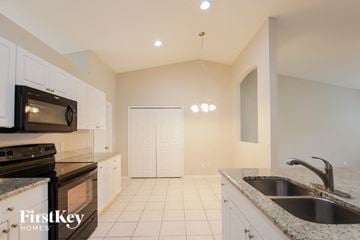 Cape Coral house for rent - a kitchen with white cabinets and black appliances and a sink