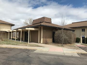 Colorado Springs apartment for rent - A building with a brown roof and beige walls with a tree in front of it.