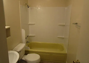 Lima apartment for rent - A white toilet sits next to a yellow bathtub in a small bathroom.