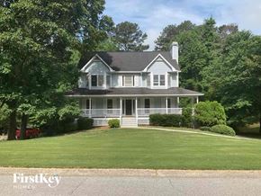 Douglasville house for rent - A white house with a black roof and a chimney is surrounded by greenery.