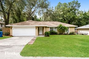 Orange City house for rent - A house with a brown roof and a white garage door is surrounded by green grass and trees.