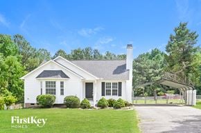 Willow Spring house for rent - A white house with a black roof and a chimney is surrounded by greenery.