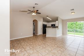 Lehigh Acres house for rent - an empty living room with a kitchen and a ceiling fan