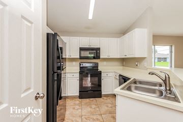 Lehigh Acres house for rent - a kitchen with black appliances and white cabinets