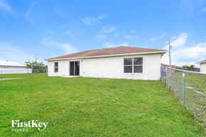 Lehigh Acres house for rent - a small white house with a grass yard and a fence