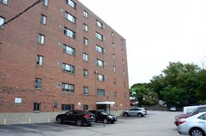Watertown apartment for rent - a tall brick building with cars parked in a parking lot