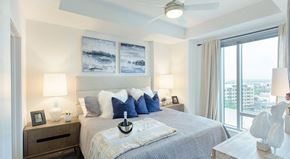 Tampa apartment for rent - A bedroom with a large bed, a ceiling fan, and a view of the city.
