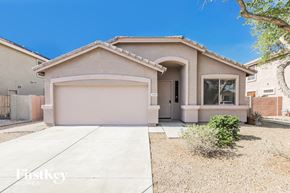 Peoria house for rent - A beige house with a garage door and a small tree in front.