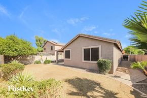 Peoria house for rent - A house with a brown roof and a white wall is surrounded by green plants and trees.