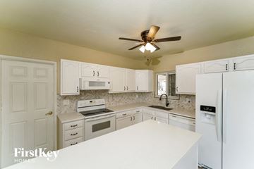 Tucson house for rent - a kitchen with white cabinets and white appliances and a ceiling fan