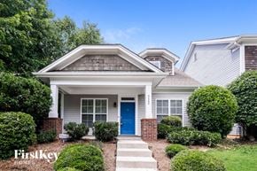 Charlotte house for rent - A house with a blue door and a brick pillar is surrounded by green bushes.