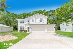 Jacksonville house for rent - A white house with a garage is surrounded by greenery and has a clear blue sky above it.